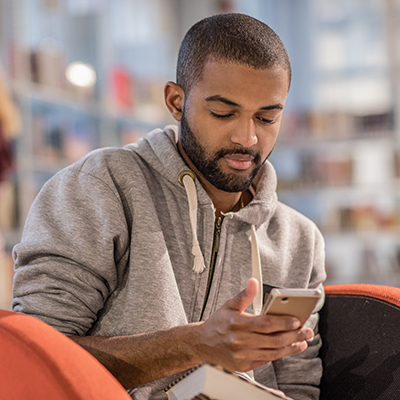 man in library with books and smart phone